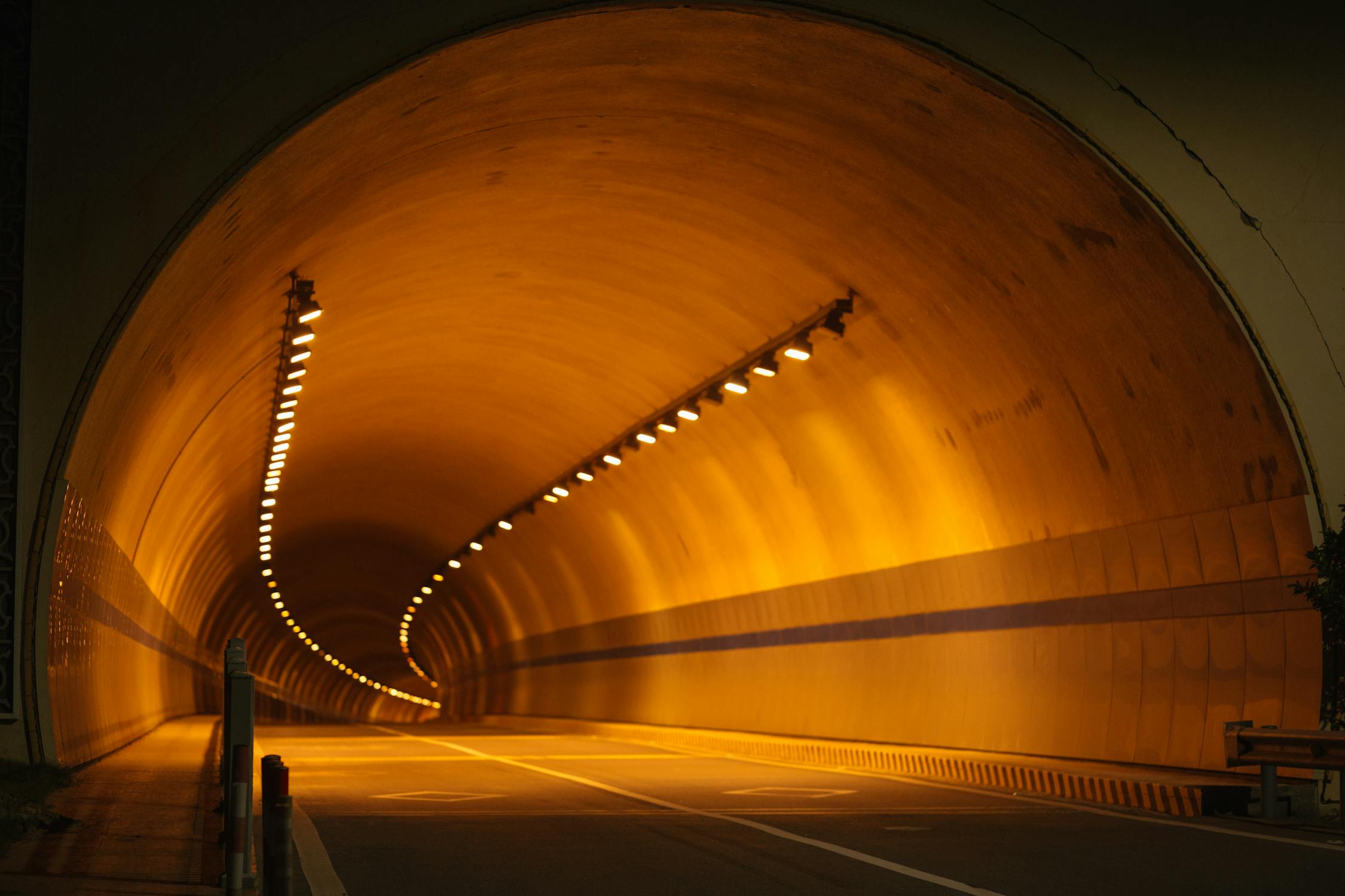 Road tunnel interior showing curved walls with rows of warm sodium vapour lighting receding into the distance